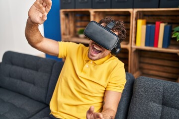 Poster - Young hispanic man playing video game using virtual reality glasses at home