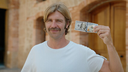 Sticker - Young blond man smiling confident holding 100 dollars banknote at street