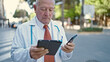© Krakenimages.com - Senior grey-haired man doctor using touchpad and smartphone at street