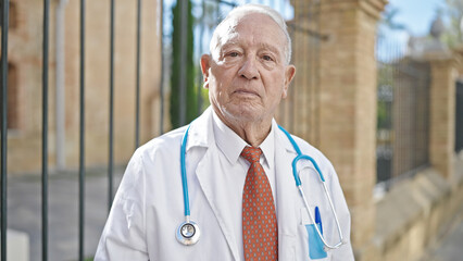 Wall Mural - Senior grey-haired man doctor standing with serious expression at street