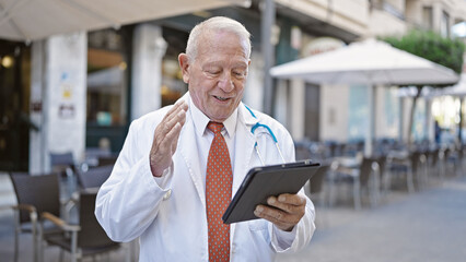 Poster - Senior grey-haired man doctor smiling confident having video call at coffee shop terrace