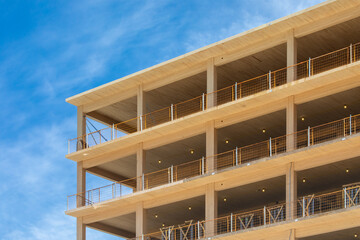 Looking up at the wooden balconys, the vertical supports and interior ceilings of a engineered timber multi story green, sustainable residential high rise apartment building construction project
