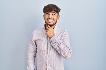 Wall Mural - Arab man with beard standing over blue background thinking worried about a question, concerned and nervous with hand on chin