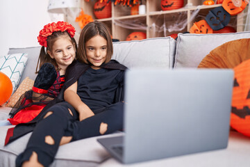 Adorable boy and girl wearing halloween costume watching movie on laptop at home