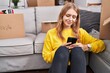 © Krakenimages.com - Young blonde woman using smartphone sitting on floor at new home