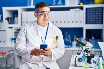 Wall Mural - Young latin man scientist smiling confident using smartphone at laboratory