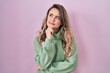 Young caucasian woman standing over pink background with hand on chin thinking about question, pensive expression. smiling with thoughtful face. doubt concept.