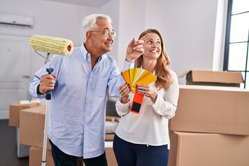 Poster - Middle age man and woman couple choosing color to paint wall at new home