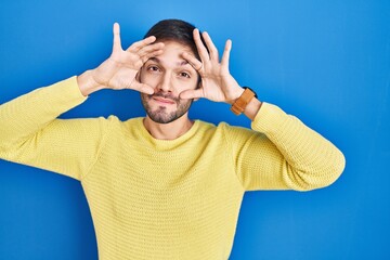 Poster - Hispanic man standing over blue background trying to open eyes with fingers, sleepy and tired for morning fatigue