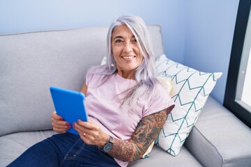 Canvas Print - Middle age grey-haired woman using touchpad sitting on sofa at home