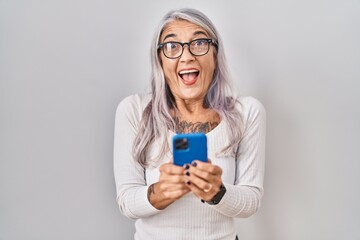 Poster - Middle age woman with grey hair using smartphone typing message celebrating crazy and amazed for success with open eyes screaming excited.