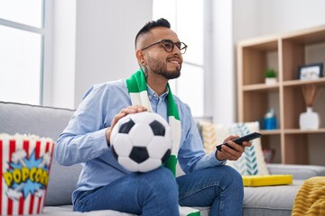 Sticker - Young hispanic man football hooligan holding ball supporting team smiling with a happy and cool smile on face. showing teeth.