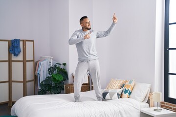 Poster - Young hispanic man standing on bed dancing at bedroom