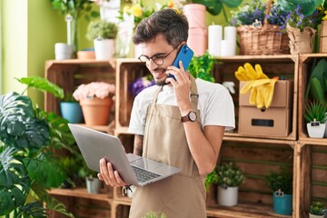 Canvas Print - Young hispanic man florist talking on smartphone using laptop at flower shop