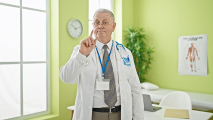 Poster - Middle age grey-haired man doctor standing with serious expression saying no with finger at clinic