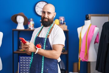 Sticker - Young bald man tailor smiling confident using smartphone at clothing factory