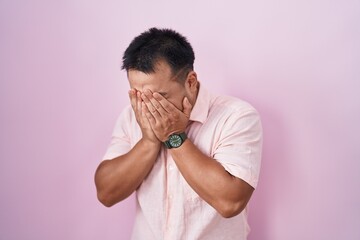 Poster - Chinese young man standing over pink background with sad expression covering face with hands while crying. depression concept.