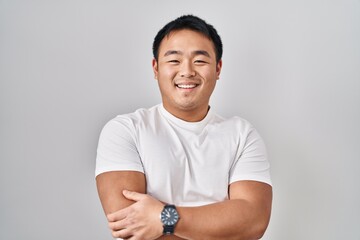 Poster - Young chinese man standing over white background happy face smiling with crossed arms looking at the camera. positive person.