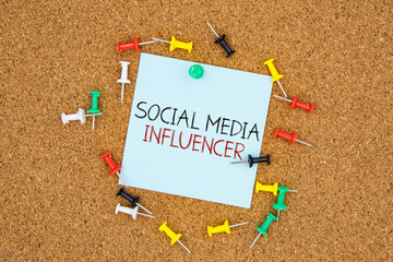 Poster - Social media influencer text on light blue post-it paper pinned on bulletin cork board surrounding by multi color pins. This message can be used in business concept about social media influencer.