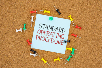 Poster - Standard operating procedure text on light blue post-it paper pinned on bulletin cork board surrounding by multi color pins. This message can be used in business concept about standard operating proce