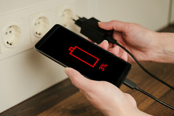 Woman hands plug charger into socket. A woman is holding a smartphone with a dead battery. Wired charging.