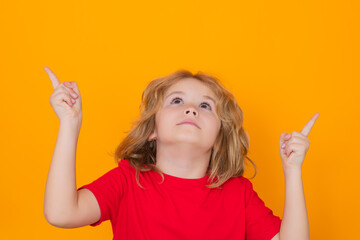 Kid pointing up finger on yellow background. Child pointing to copyspace, showing promo offers, points up.