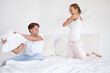 Fun, energy and couple fighting with pillows on the bed in hotel room on a romantic weekend trip. Happy, love and young woman and man laughing, bonding and playing together in the morning in bedroom.