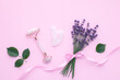 Quartz face roller on pink background, top view. Facial massage tool. Skin care, treatment concept. Gua sha massager made from natural jade and rose stone. Lavender flowers bouquet tied with ribbon.