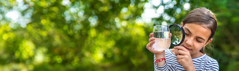 The child examines the water with a magnifying glass. Selective focus.