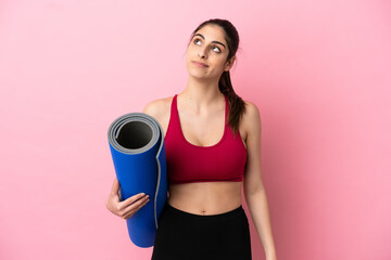 Wall Mural - Young sport caucasian woman going to yoga classes while holding a mat and looking up