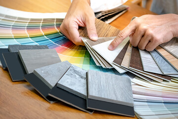 Wall Mural - Designer hand choosing and pointing at wood laminate material samples with color swatch and wooden tile texture collection nearby. Catalog guide for interior architecture and furniture design work