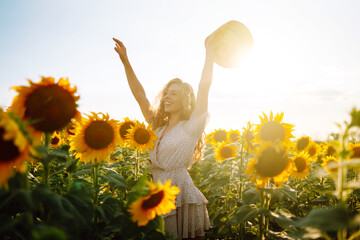 Beautiful woman posing in a field of sunflowers in a dress and hat.  Fashion, lifestyle, travel and vacations concept.