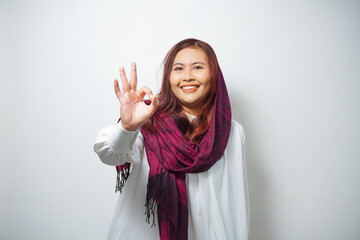 Portrait of a smiling Asian Muslim woman, giving an OK hand gesture isolated over white background