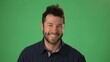 © Robert Peak - Handsome dreamful bearded young guy 20s in hoodie isolated on green screen chroma key background in studio. People sincere emotions, lifestyle concept. Smiling looking at the camera.