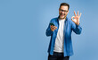 Portrait of satisfied businessman using smart phone and showing OK gesture against blue background