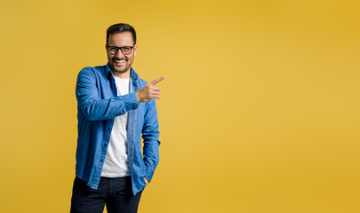 Smiling male entrepreneur pointing at copy space for marketing while standing on yellow background