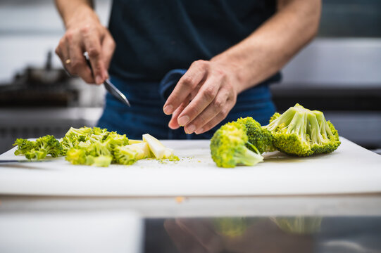 Close-up of a cook's hands cutting broccoli in a restaurant.