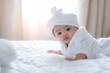 © Wanwajee - Adorable baby child looking away through camera on white bed, with curtain background and light of rising sun.