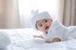 © Wanwajee - Baby child lie on stomach with head up, cute infant on white bed with blur white curtain and light of morning.