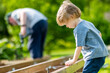 Cute toddler boy helping his grandfather. Senior man working on a project in his garden.