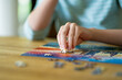 © MNStudio - Close-up on woman hand playing puzzles at home. Connecting jigsaw puzzle pieces in a living room table, assembling a jigsaw puzzle.