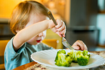 Wall Mural - Cute toddler boy eating broccoli. First solid foods. Fresh organic vegetables for infants. Healthy nutrition for the family.