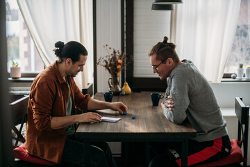 Two young men are playing dice at a table in the living room at home