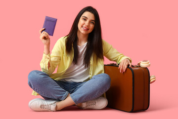 Canvas Print - Young woman with passport and suitcase sitting on pink background