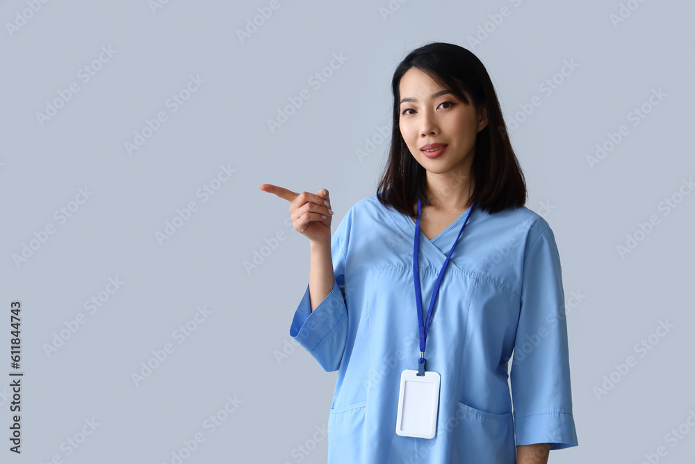 Female Asian medical intern pointing at something on grey background