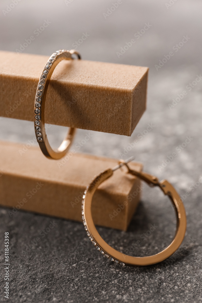 Decorative podium with beautiful golden earrings on grunge grey background