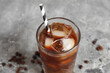Glass of ice coffee with straw and beans on grey grunge background