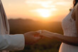 The bride and groom use the little finger together, lovely couple hold hand with sunset background