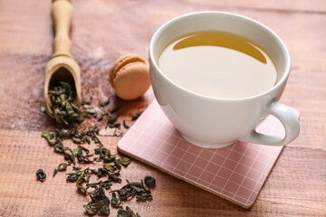 Wall Mural - Drink coaster with cup of tea, macaroon and scattered leaves on wooden table, closeup