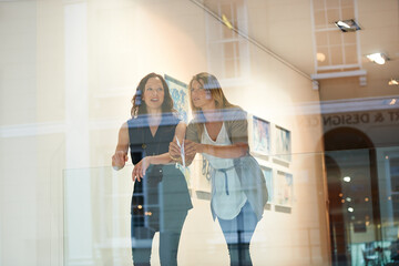 Women, friends together and exhibition at gallery, conversation and culture appreciation. Woman, art critic partnership and looking in museum with talk, lifestyle and ideas by window with reflection